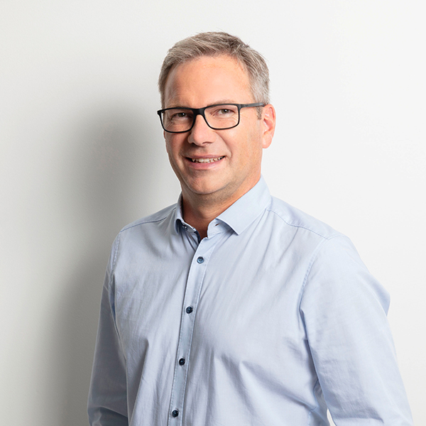 Portrait of a man wearing glasses and a light-blue button-down shirt, smiling at the camera.