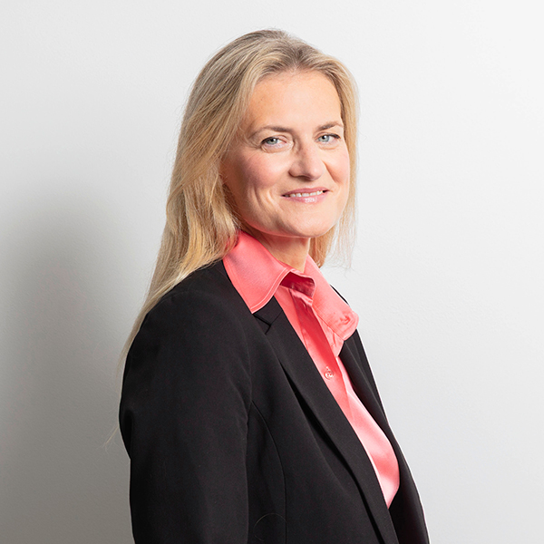 Professional portrait of a smiling woman in a black blazer and pink blouse, facing slightly to the right against a light background.