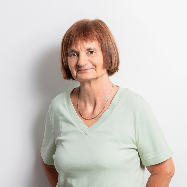 Smiling older woman with short brown hair wearing a light green V-neck shirt against a white background.