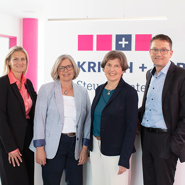 Four business professionals standing side by side in a bright office with a company logo on the wall behind them
