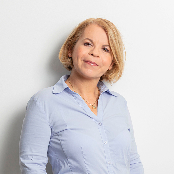 Portrait of a smiling woman with short blonde hair wearing a light blue button-down shirt against a light background.